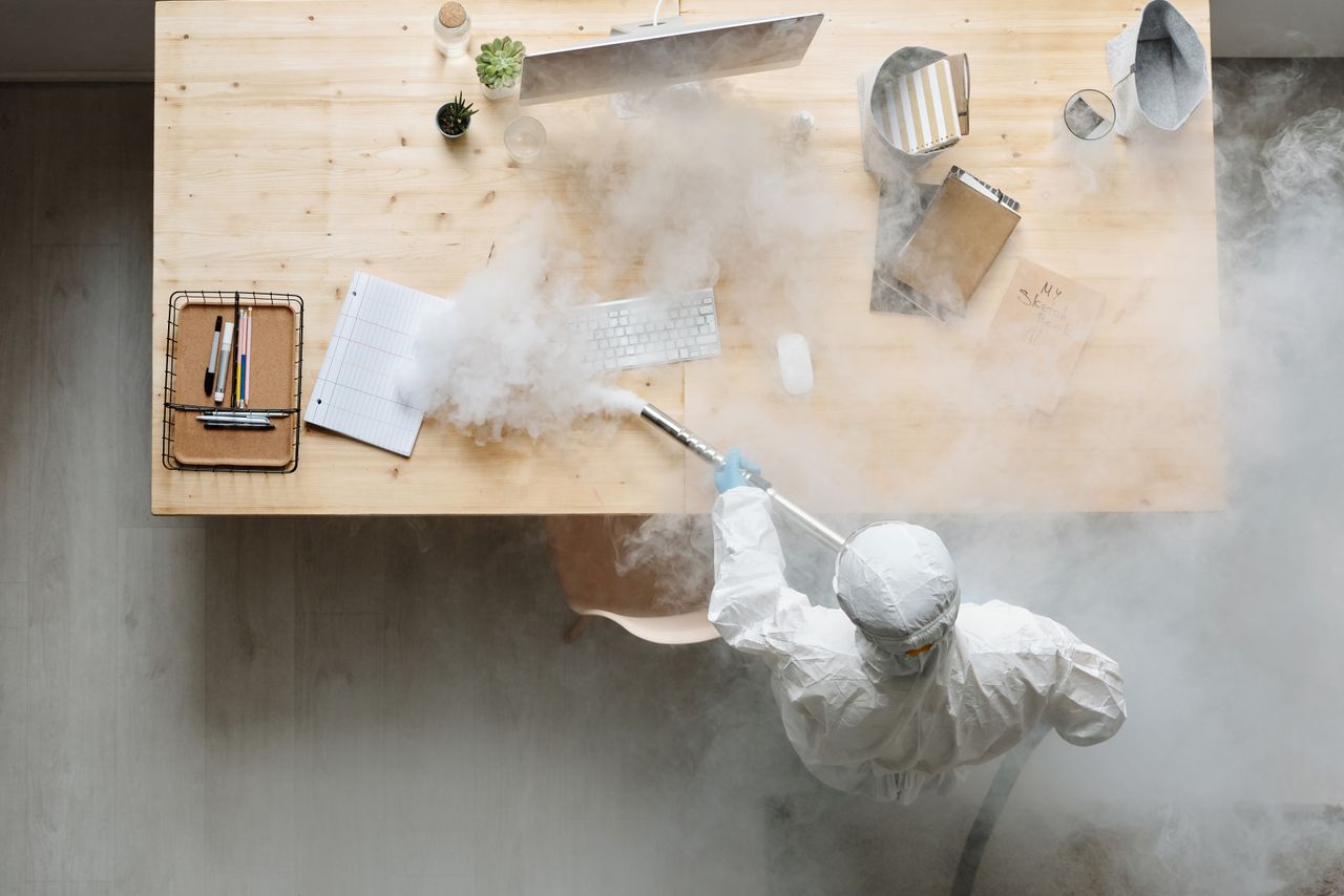A person disinfects a work area by fumigation while wearing full protective equipment for safety.